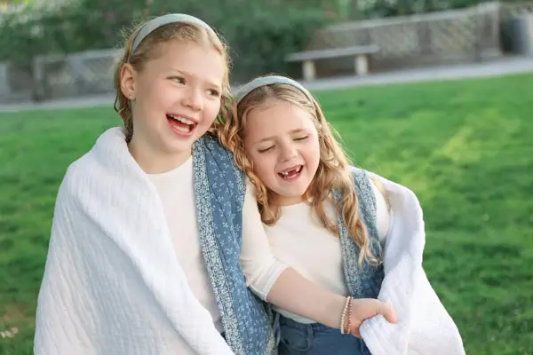 Two laughing sisters wrapped in a blanket on the grass, outdoor photography by Photoholic, Rockland County NY